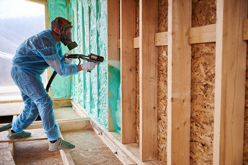 Worker spraying polyurethane insulation in wall cavity
